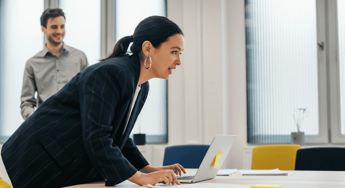 Business owner leaning over a laptop, reviewing results with a colleague.